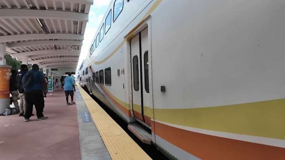 Plataforma vazia de estação do trem SunRail em Orlando, com céu azul, palmeiras e luz solar típica da Flórida