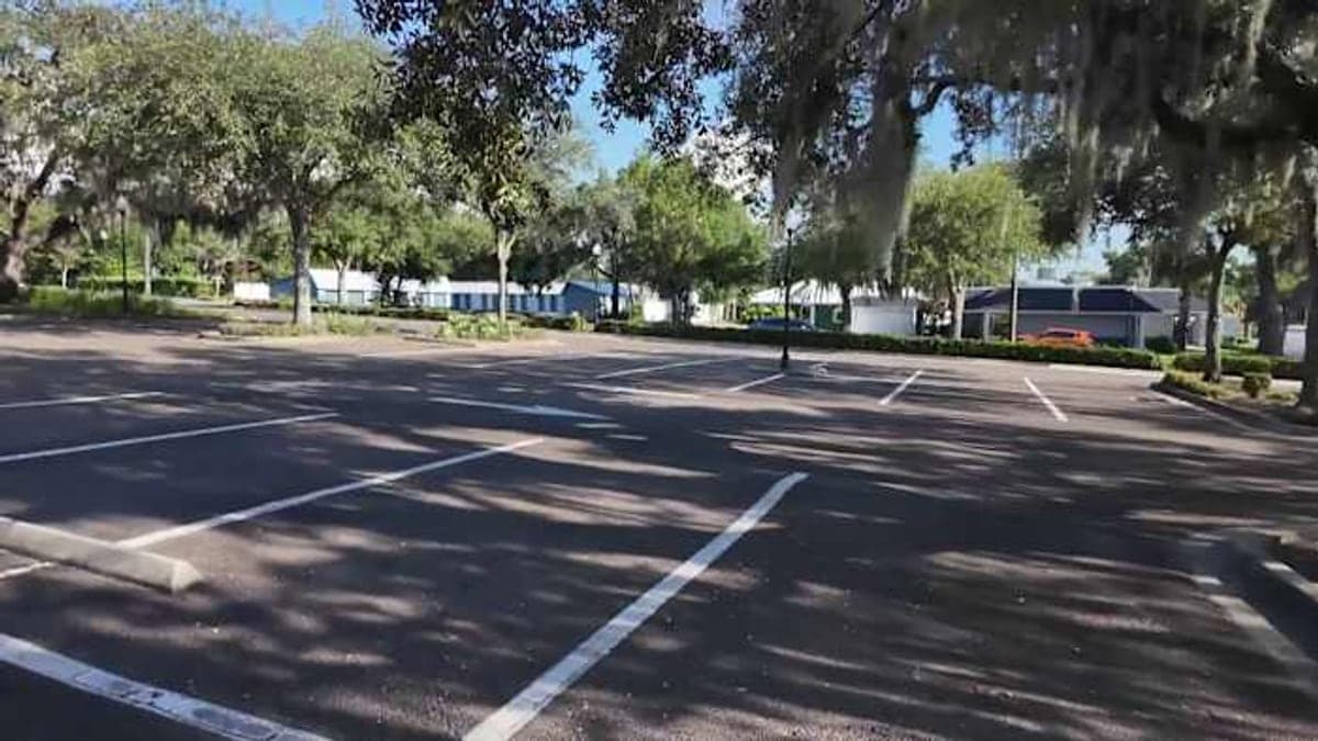 Vista da interseção da 7th Street com a Minneola Avenue no centro de Clermont, mostrando estacionamentos públicos, prédios comerciais baixos e árvores sob sol forte.