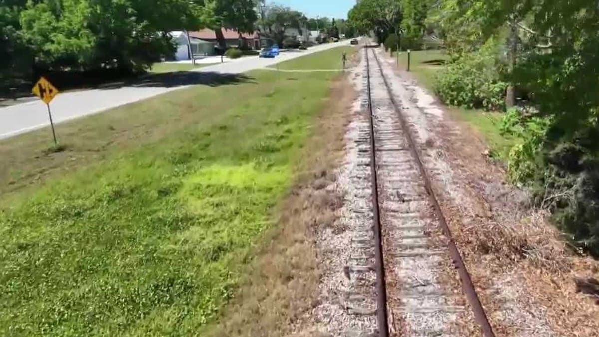 Trecho de ferrovia desativada em área suburbana da Flórida com árvores e gramado ao redor, céu claro