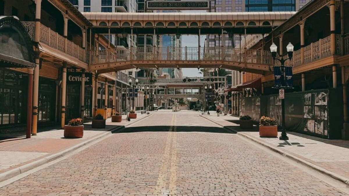 Rua no centro de Orlando com prédios baixos de estuque e telhados de metal, palmeiras e céu azul com nuvens.