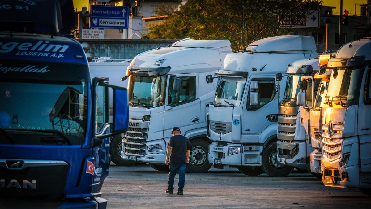 Homem caminhando entre vários caminhões estacionados em um pátio ao entardecer
