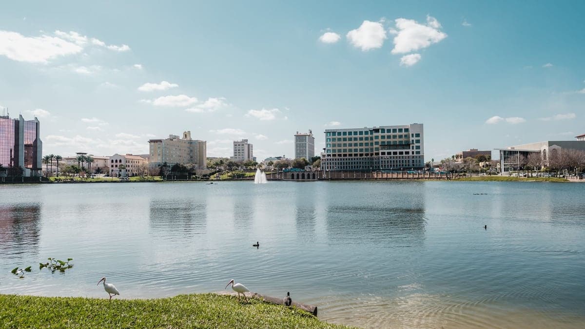 Vista panorâmica do centro da cidade de Kissimmee com prédios e um lago ao fundo sob céu azul com algumas nuvens