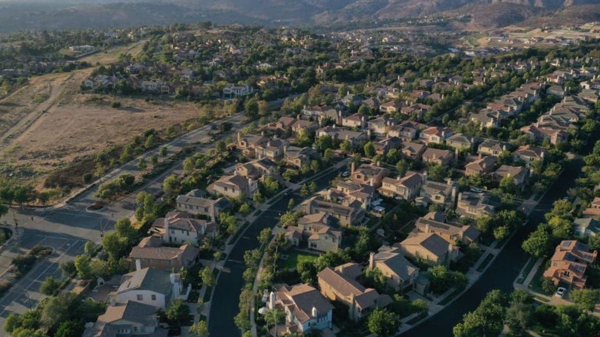 Foto aérea de um bairro residencial com casas unifamiliares, ruas e áreas verdes em um dia ensolarado