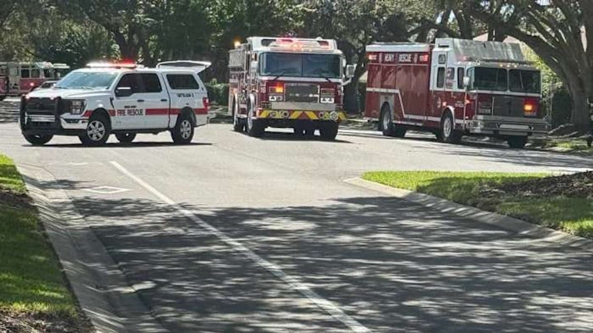 Cruzamento de rua em bairro residencial com casas, calçadas e vegetação típica da Flórida sob céu claro