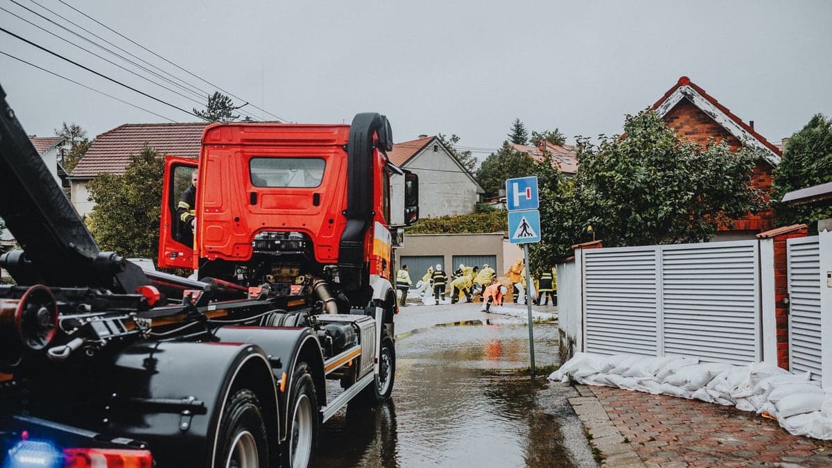 Caminhão de resgate em rua alagada com equipe de emergência ao fundo e casas ao redor