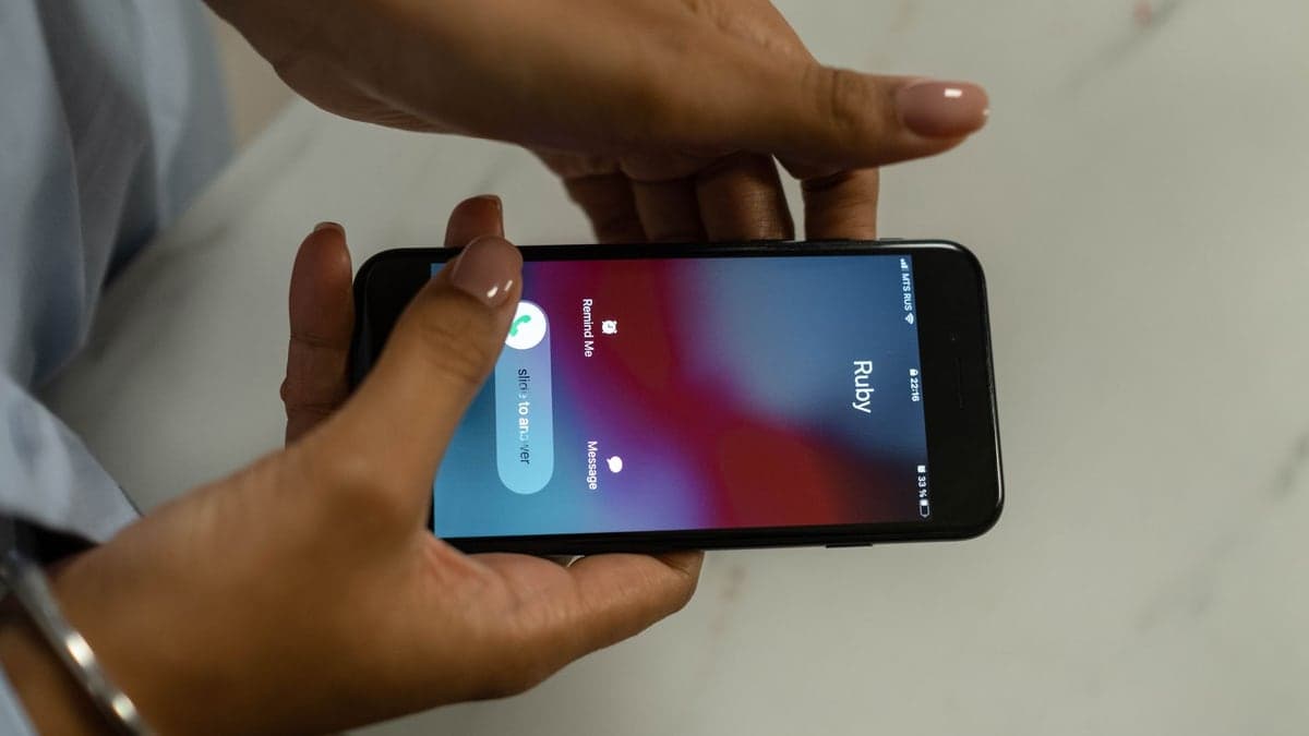 Mãos segurando um celular com uma chamada recebida no visor, exibindo o nome 'Ruby' e opções para aceitar ou recusar a chamada.