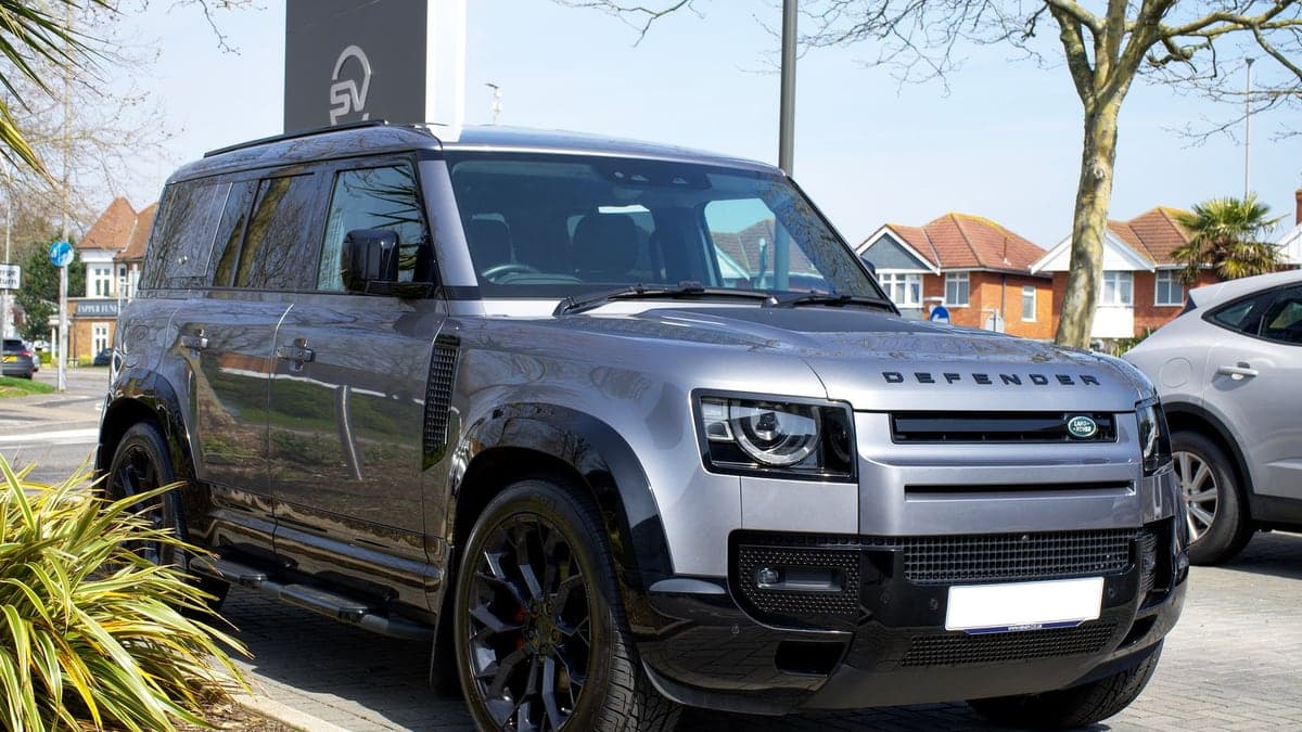 Foto de um carro SUV cinza estacionado em ambiente externo com árvores e casas ao fundo