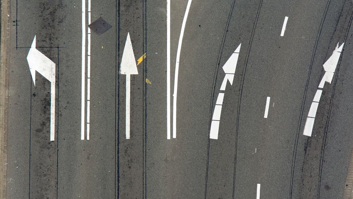 Foto aérea mostrando setas pintadas no asfalto indicando faixas exclusivas para conversão à esquerda, em frente e à direita em uma via.