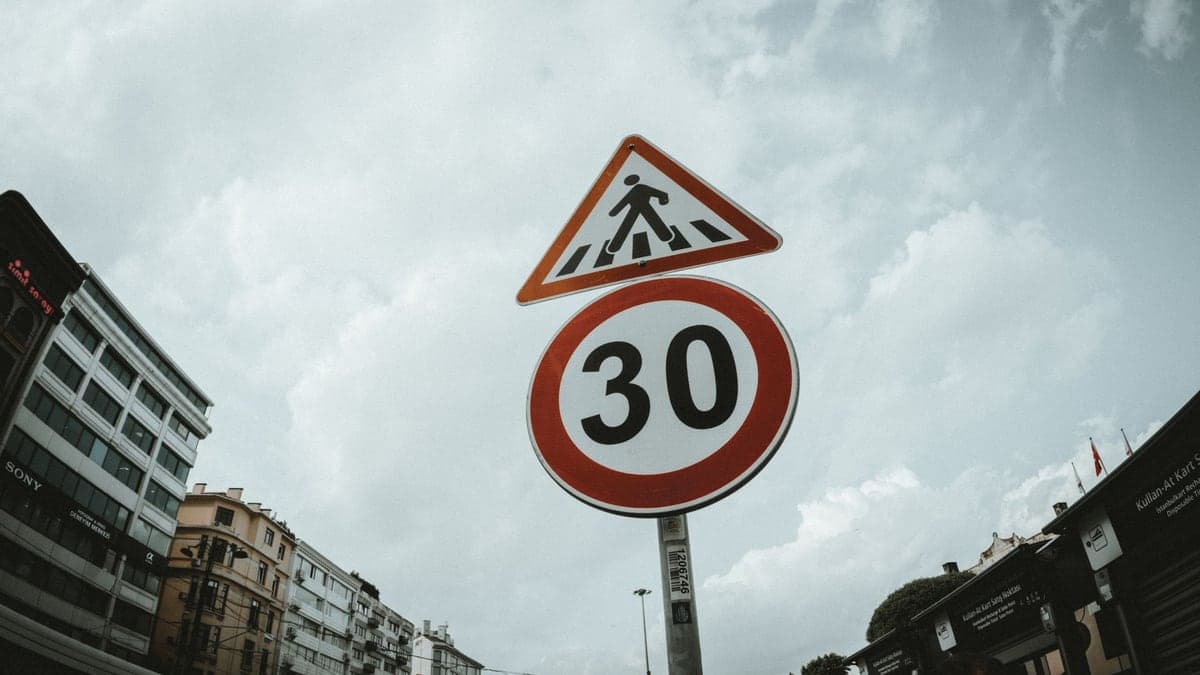 Placa de trânsito triangular com símbolo de faixa de pedestres e placa circular com limite de velocidade 30 km/h em área urbana