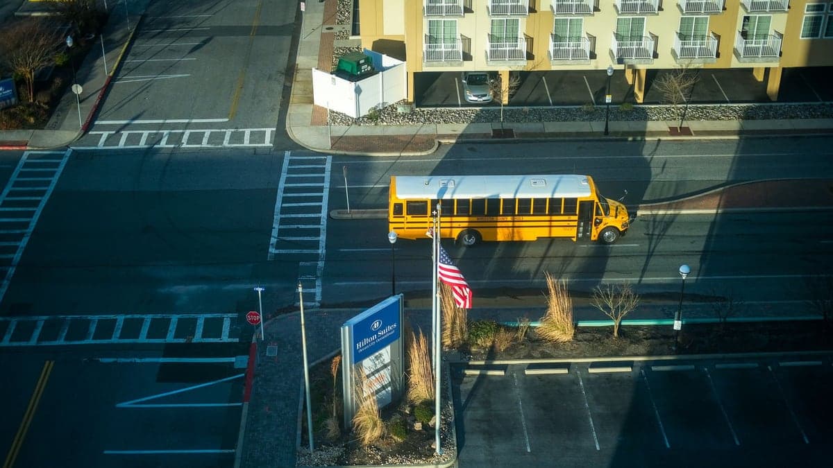ônibus escolar amarelo parado em cruzamento de rua visto de cima com sombra de outro veículo próximo