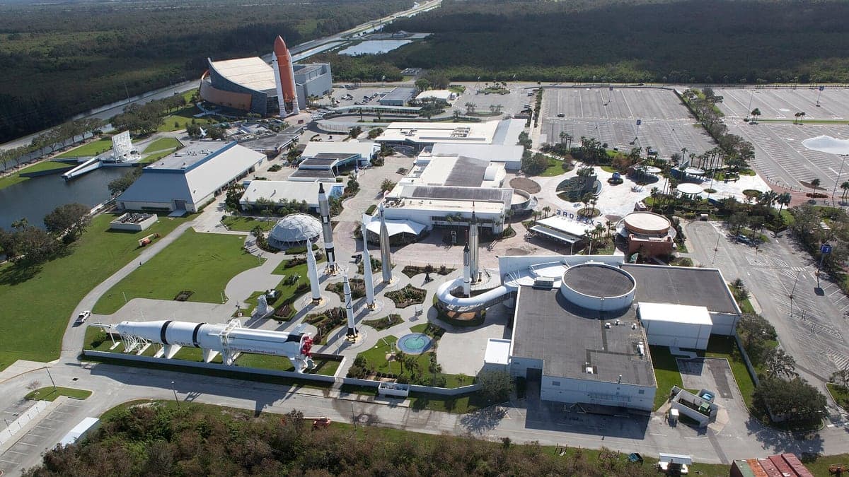 Vista aérea do Kennedy Space Center com prédios, foguetes em exibição e áreas de estacionamento vazias