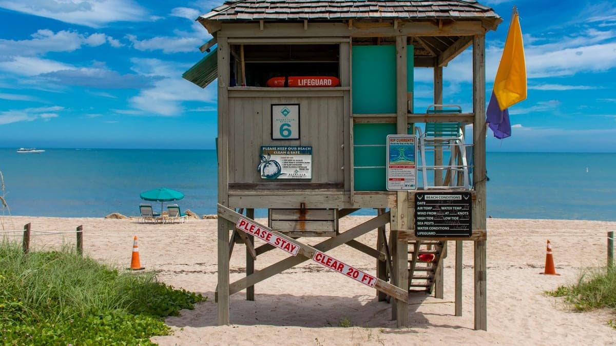 Torre de salva-vidas na praia com bandeira amarela e roxa indicando alerta de risco no mar, com o mar calmo ao fundo