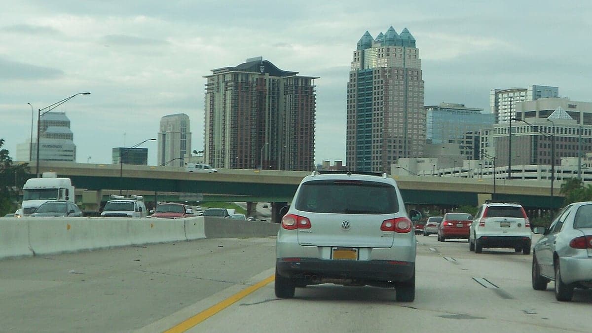 Vista da estrada I-4 com carros trafegando e prédios altos do centro de Orlando ao fundo, sob um céu nublado