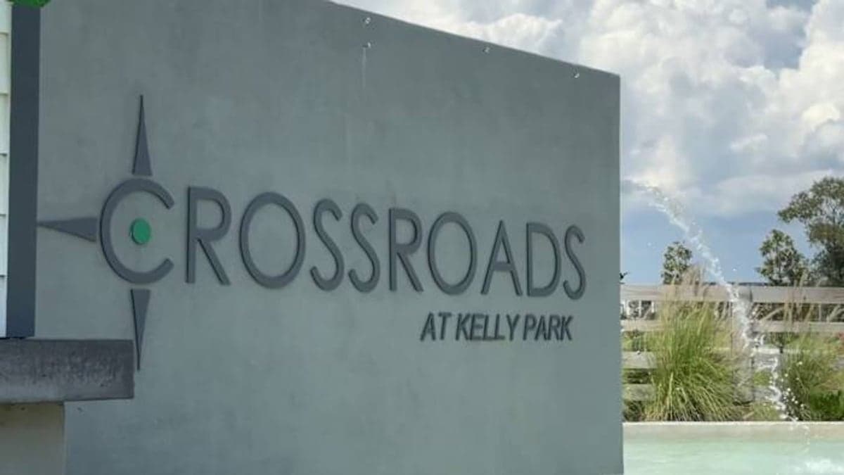 trecho de uma estrada suburbana com prédios baixos, palmeiras e carvalhos próximos sob céu claro, mostrando a área onde a Kelly Park Road está localizada