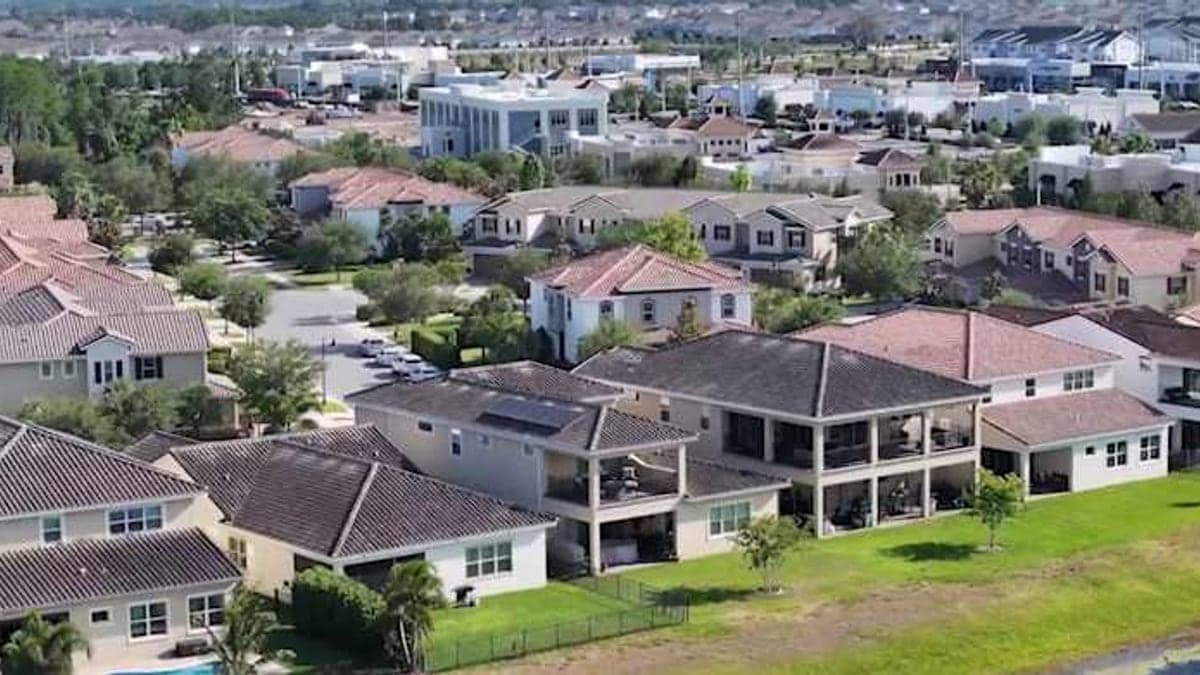 Vista de uma estrada suburbana no sudeste de Orlando, com trânsito moderado, palmeiras e prédios baixos sob céu ensolarado