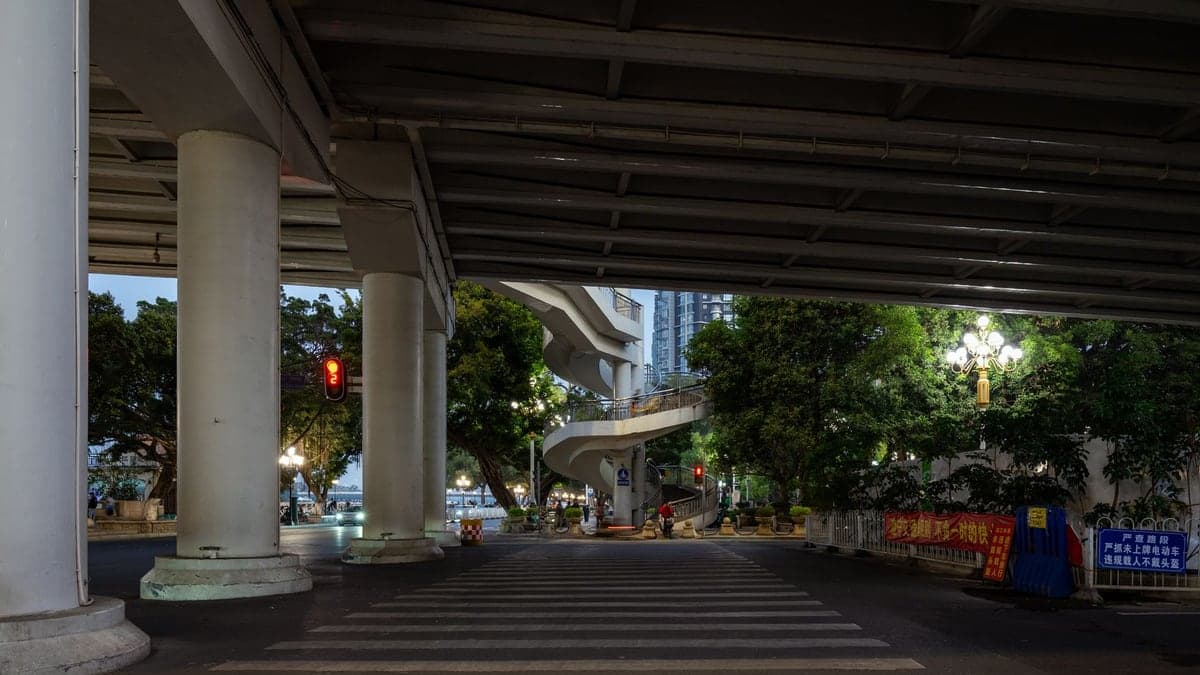 Área sob uma grande via elevada com colunas e faixa de pedestre em primeiro plano à noite