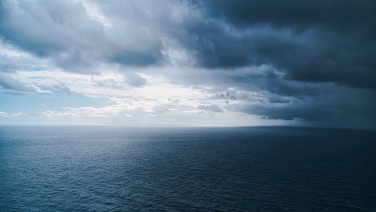 Oceano sob céu nublado com nuvens escuras indicando tempestade à distância