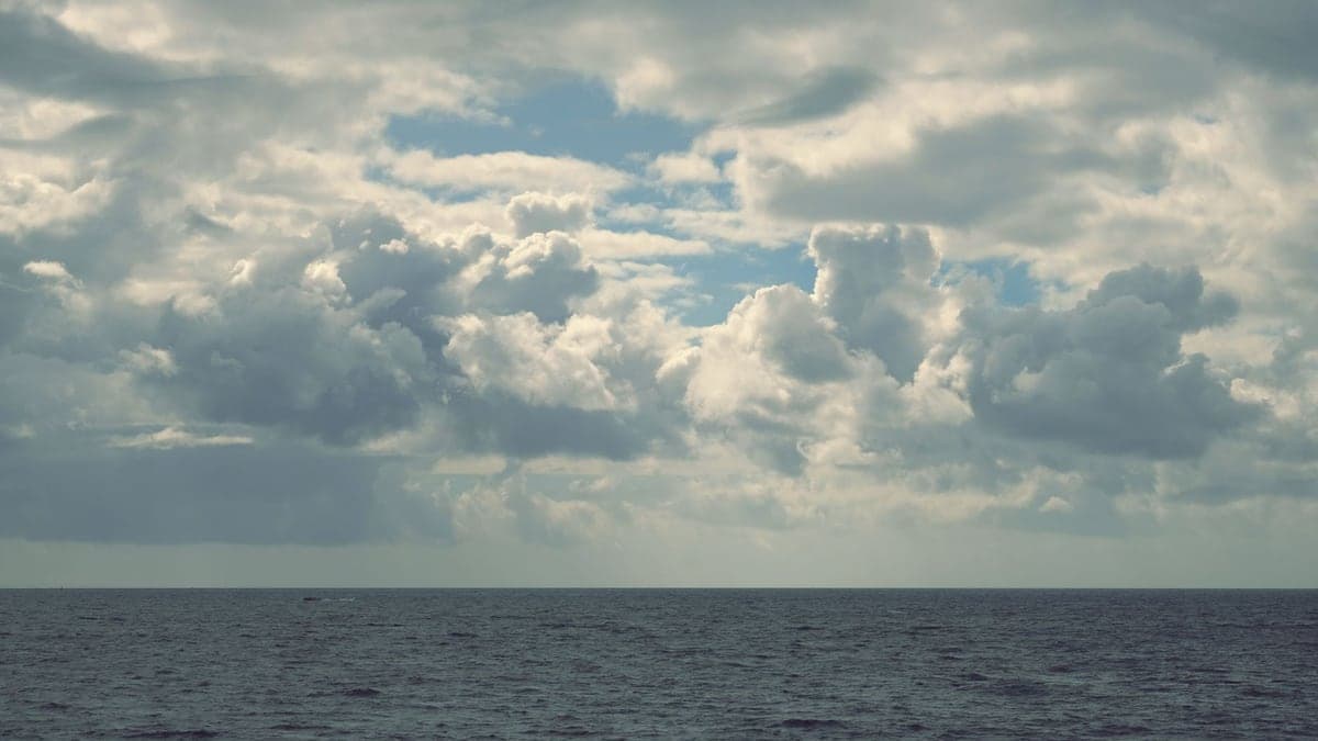 Mar oceânico com céu parcialmente nublado, nuvens densas no horizonte acima do mar calmo.