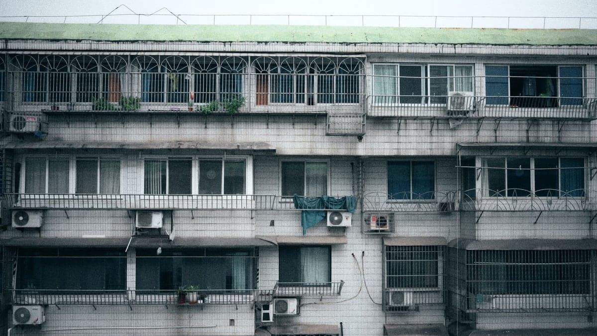 Fachada de edifício baixo com paredes pintadas em verde e laranja, com duas janelas e aparelhos de ar-condicionado instalados em algumas delas.