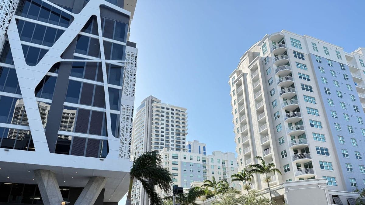 Rua urbana com prédios altos e barreiras de trânsito com placas de proibido passar sob céu azul