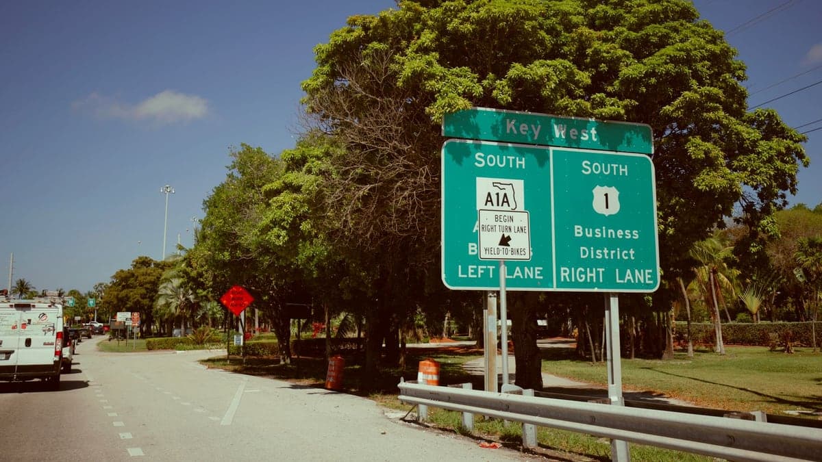Vista de rua em Mount Dora com árvores altas ao lado da via e placas de sinalização de direção para Key West e Business District.