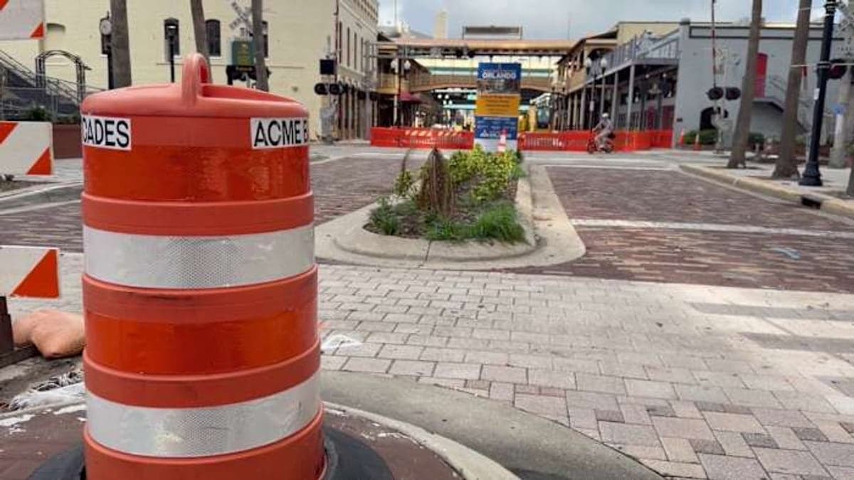 Rua com calçadas e faixas para veículos no centro de Orlando, com árvores e edifícios baixos ao redor sob céu azul