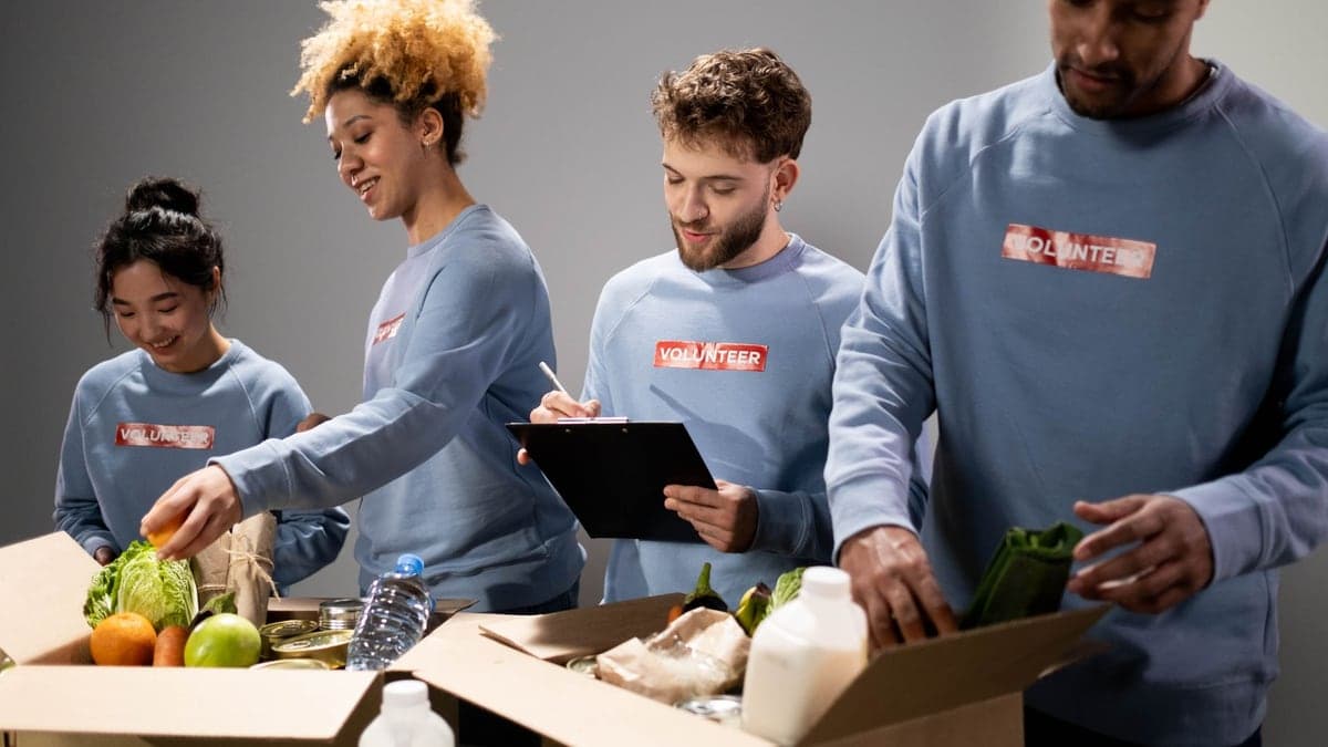 Quatro voluntários embalando alimentos frescos em caixas para doação, em ambiente claro e organizado.