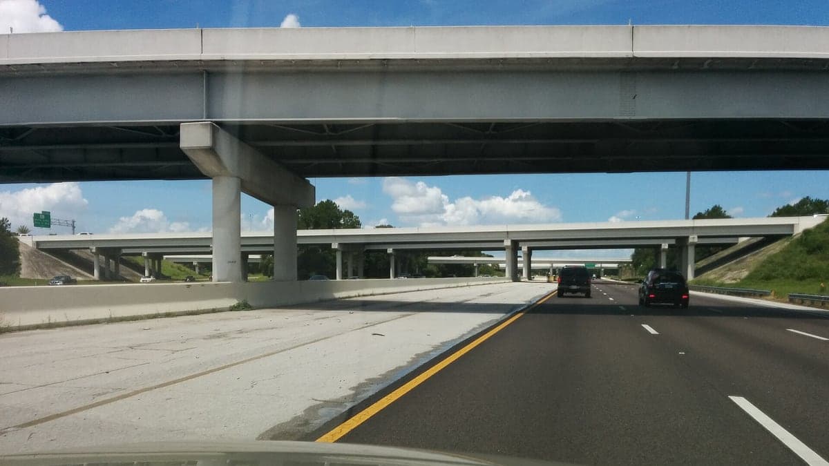 Foto da interestadual I-4 com viadutos e algumas poucas carretas com céu azul e poucas nuvens no horizonte.