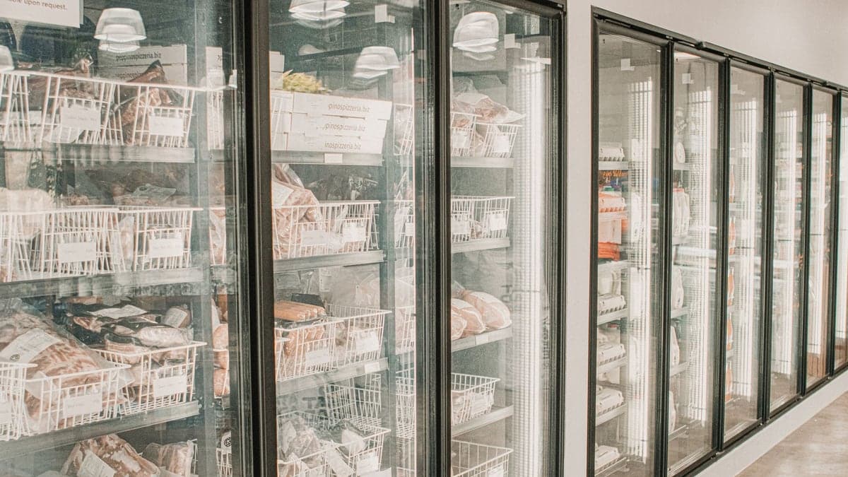 Corredor de supermercados com vários freezers verticais contendo alimentos congelados.