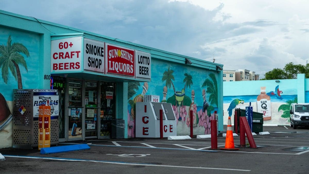 fachada de um comércio colorido com letreiros de loja de bebidas e estacionamento à frente