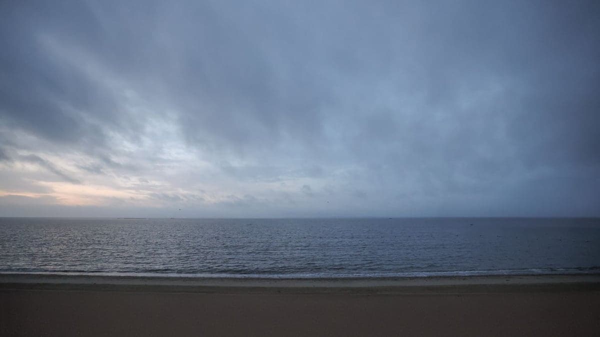 Mar e céu nublado ao entardecer com tons cinzas, mostrando uma linha de horizonte tranquila e sem praia visível
